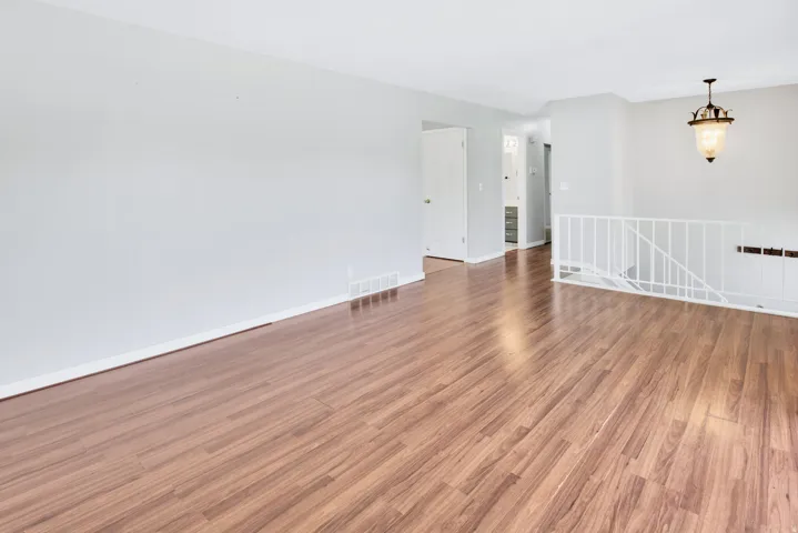 Wood-finish flooring, white walls, white railing, and a decorative pendant light fixture