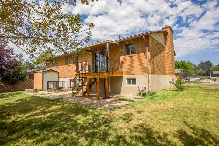 Rear exterior featuring brick siding, a raised wood deck with metal railing, a ground-level patio, and a storage shed