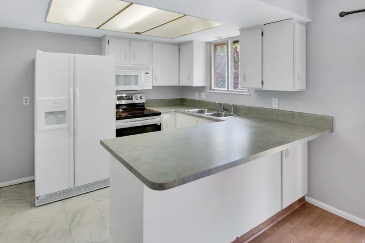 Kitchen featuring white cabinetry, a double basin sink, a built-in microwave, and a breakfast bar