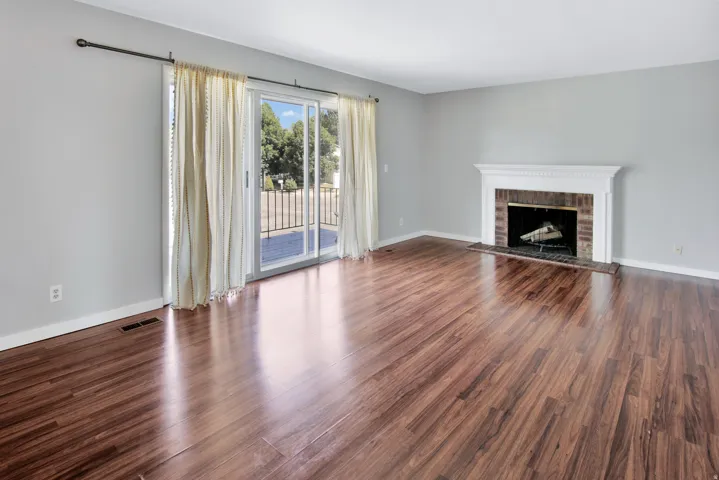Wood-finish flooring, brick fireplace with a white mantel, and sliding glass doors to the exterior