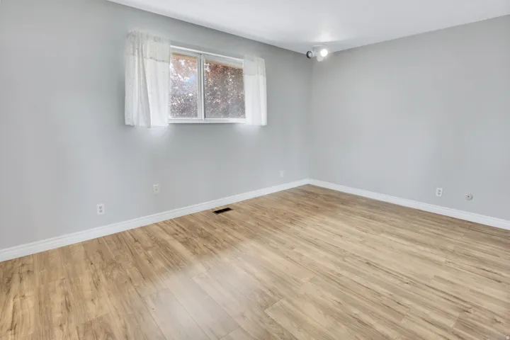Wood-finish flooring, light gray walls, white trim, and a window with white casing