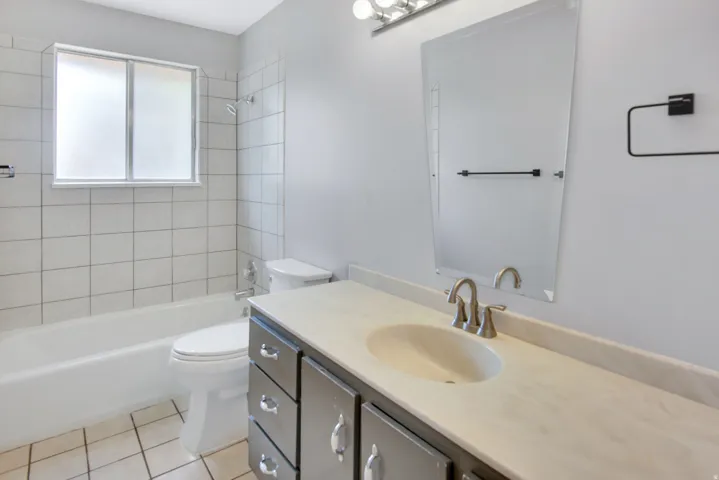 Full bathroom featuring a single vanity with an integrated sink, a rectangular mirror, and a tub with tiled walls