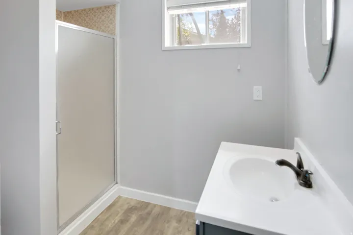 Enclosed shower with patterned wall tile, vanity with integrated sink, dark-toned faucet, and wood-finish flooring