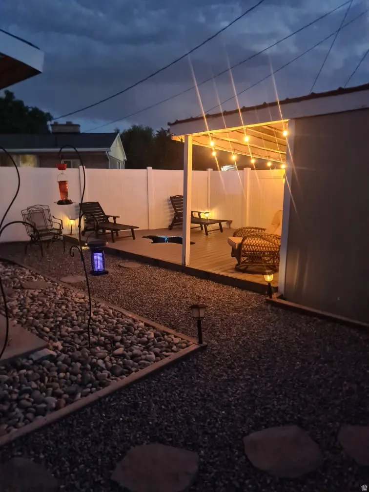 Covered patio structure with string lighting, privacy fencing, and a gravel pathway