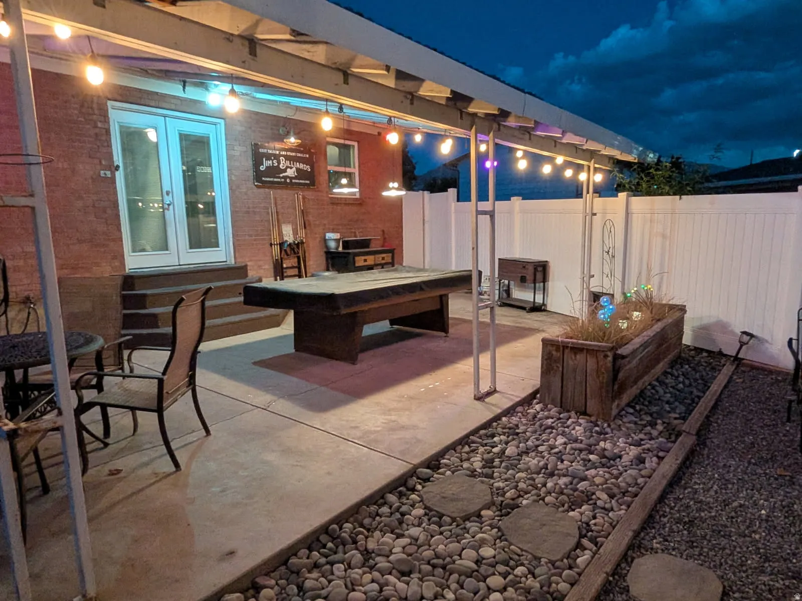 Brick exterior with double doors, concrete patio, white privacy fencing, and a decorative rock border