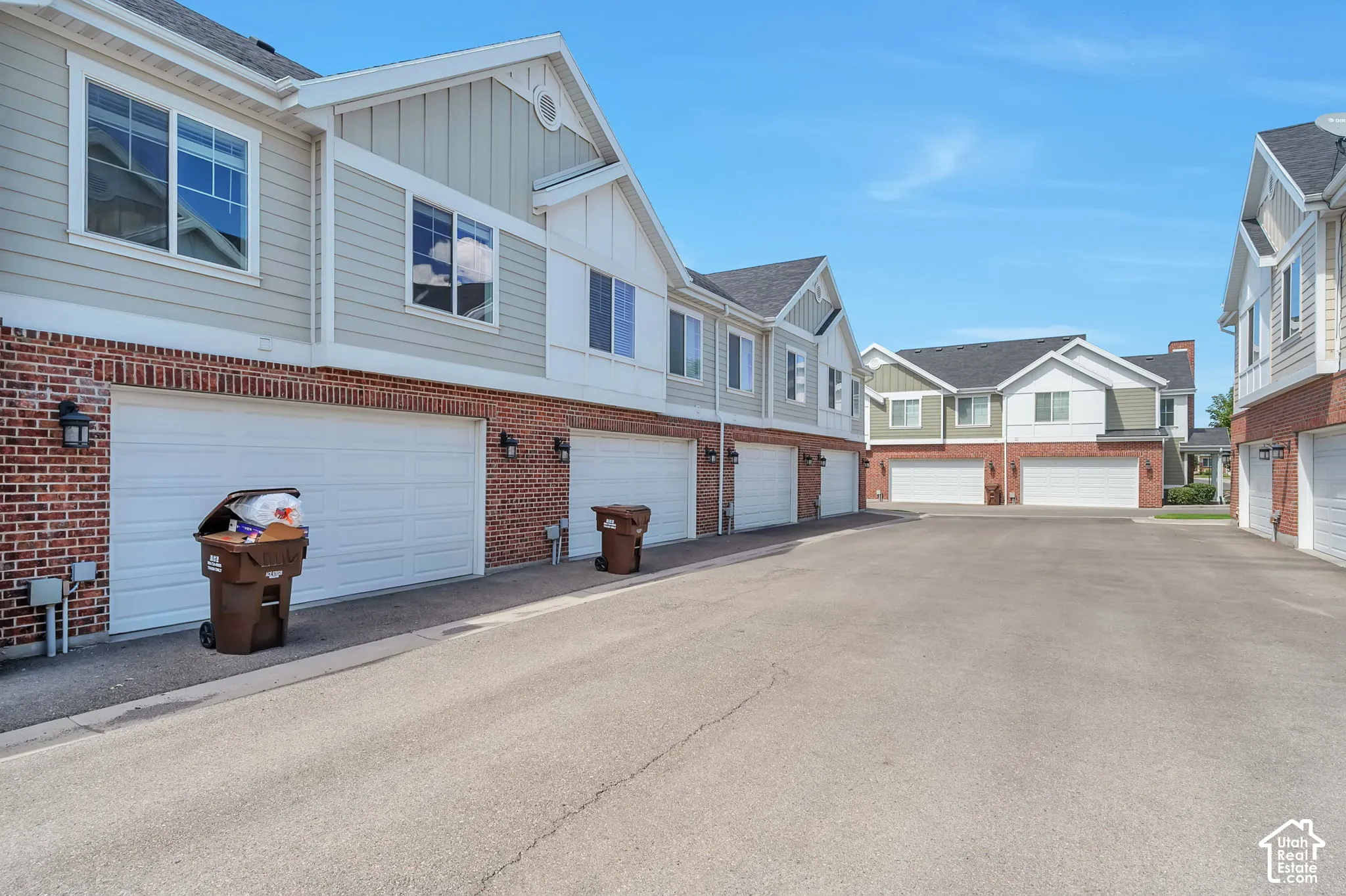 Two-story townhome exteriors featuring brick and siding finishes, individual garage doors, and ample paved driveway space