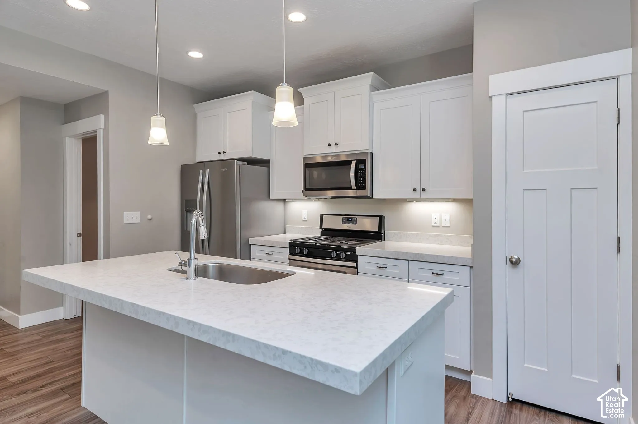 Central kitchen island with an undermount sink, white shaker cabinetry, stainless steel appliances, and pendant lighting
