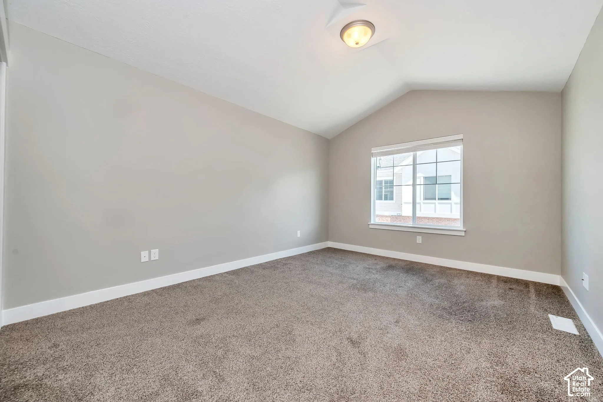 Vaulted ceiling, neutral wall paint, carpeted flooring, large window with grid pattern, and white trim