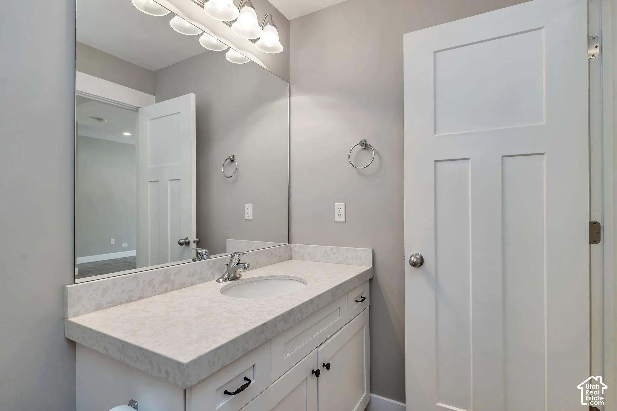 White vanity with a light-colored countertop, undermount sink, wall-mounted mirror, and overhead light fixture