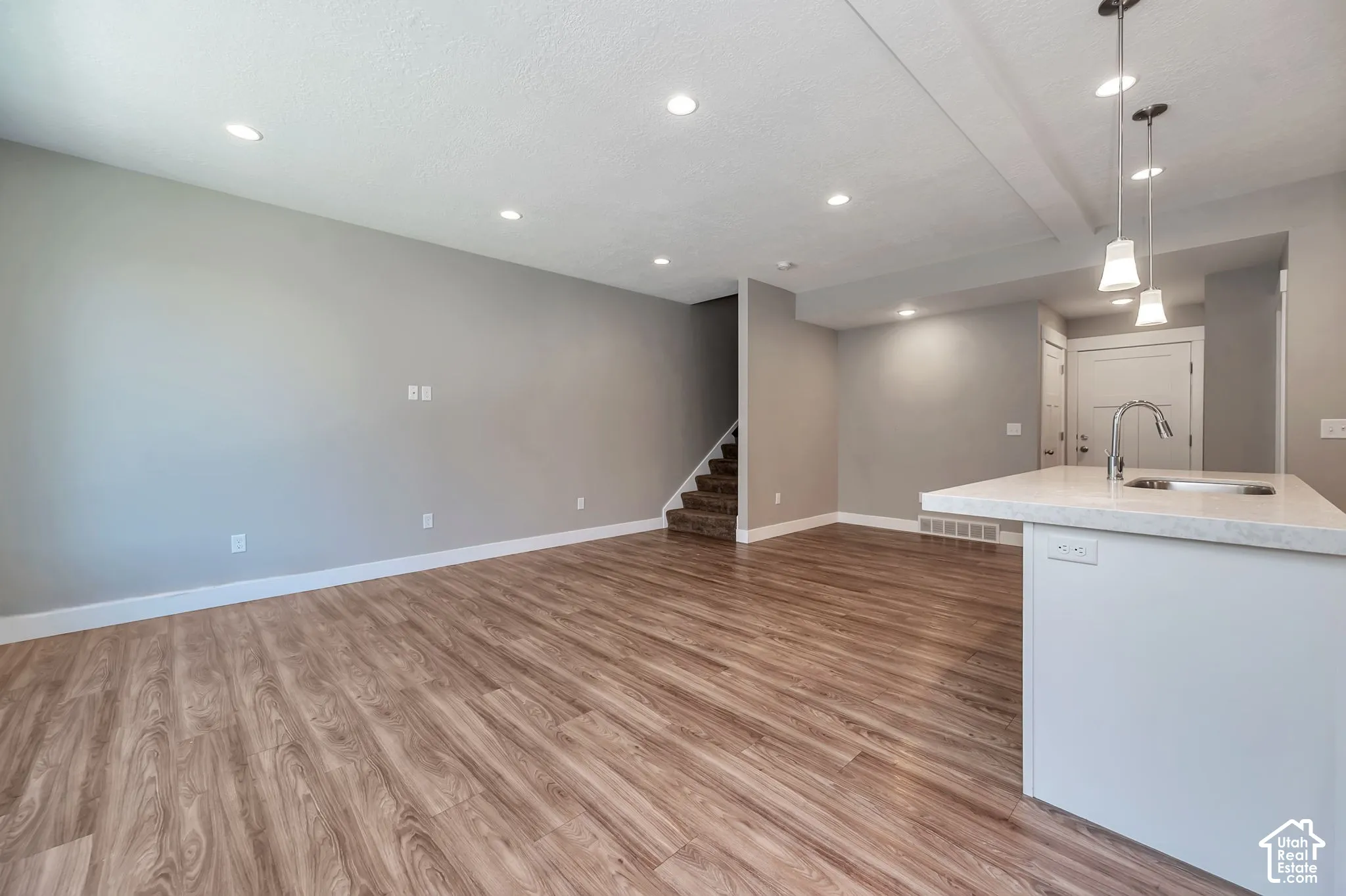 Open concept living space featuring wood-finish flooring, recessed lighting, and a kitchen island with a built-in sink