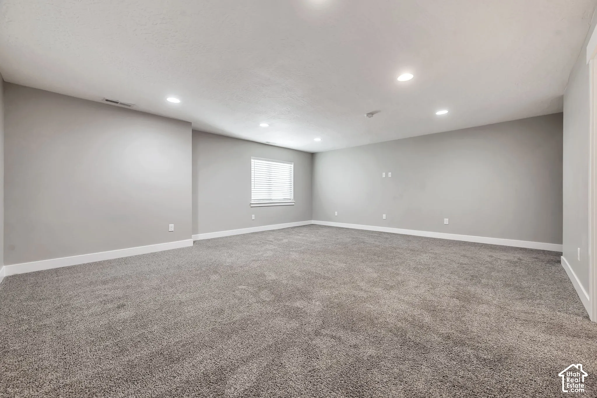 Expansive room featuring plush grey carpeting, light grey wall finishes, and recessed ceiling lighting