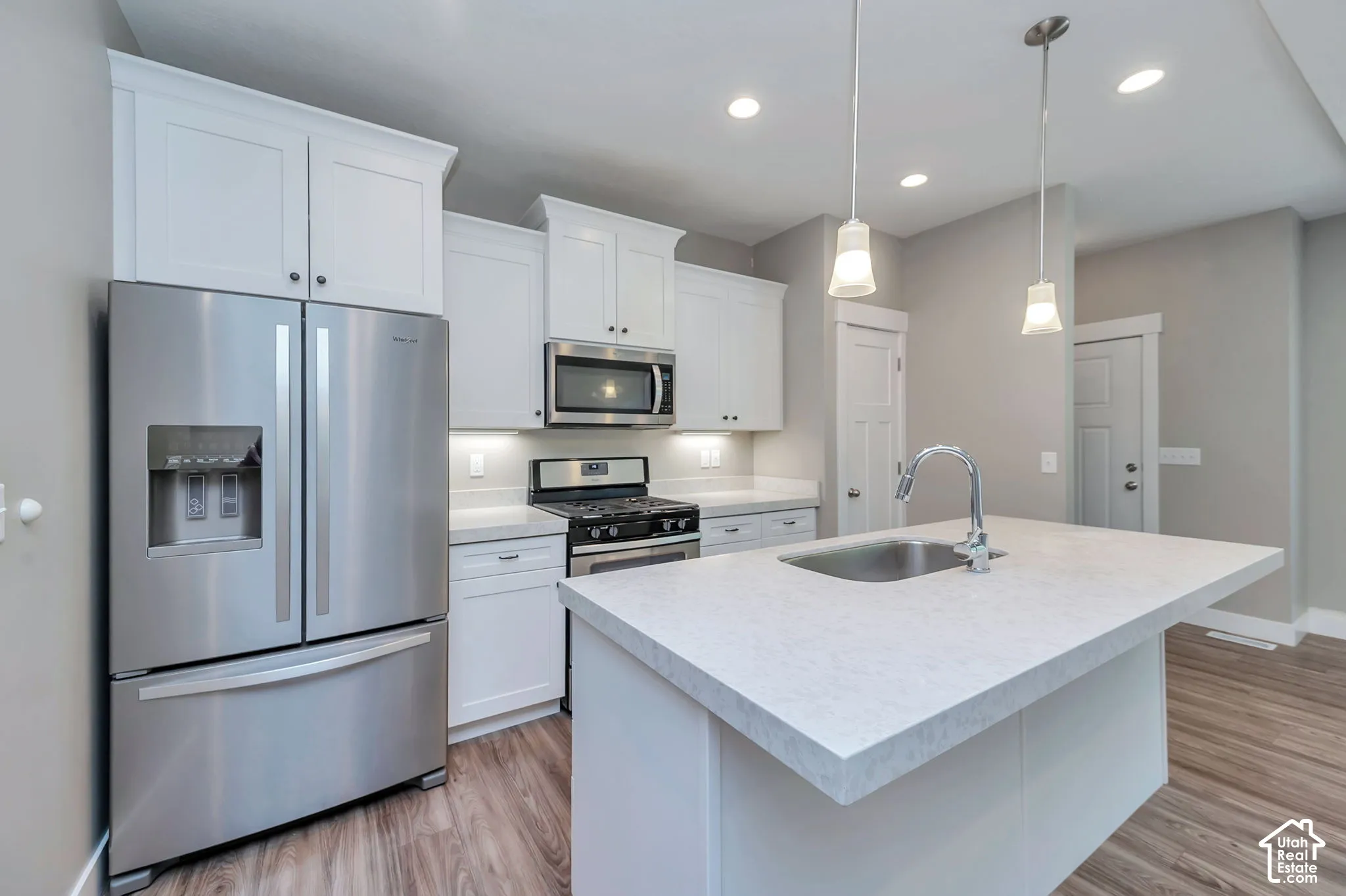 Kitchen featuring stainless steel appliances, white cabinetry, a kitchen island with an integrated sink, pendant lighting, and recessed ceiling lights