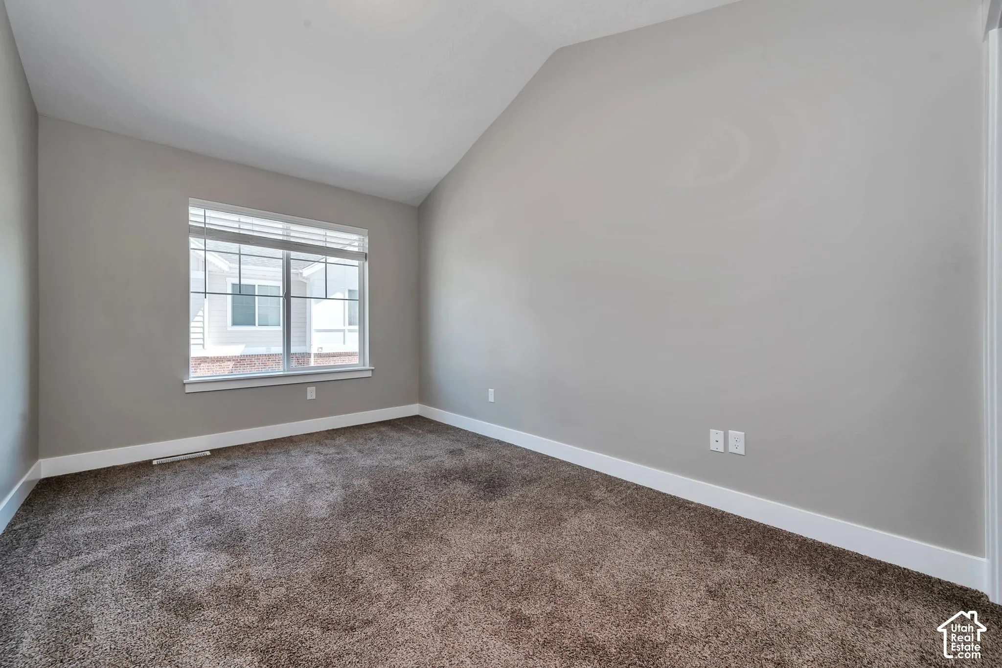 Vaulted ceiling, neutral wall tones, large window with blinds, plush carpeting, and white trim