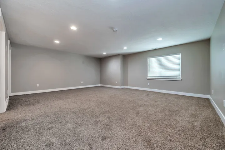 Spacious room with plush carpeting, recessed lighting, neutral wall tones, and a window with blinds