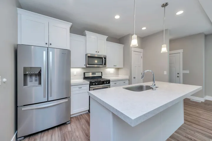 Kitchen featuring stainless steel appliances, white cabinetry, a kitchen island with an integrated sink, pendant lighting, and recessed ceiling lights