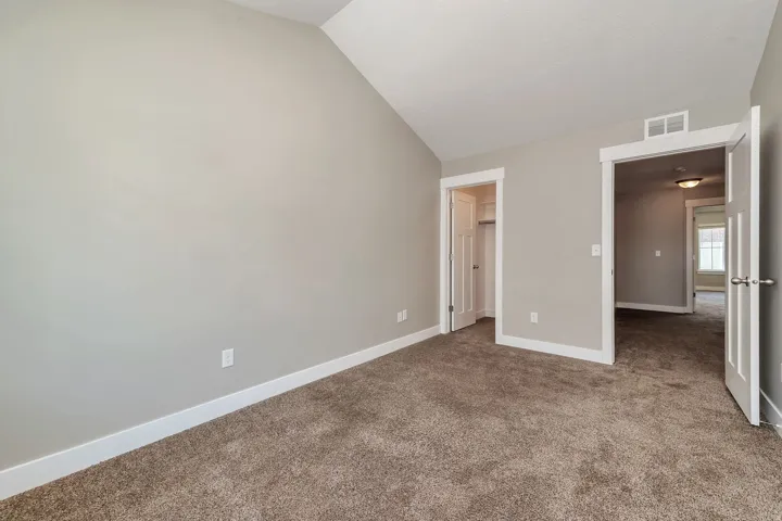 Vaulted ceiling, neutral wall paint, plush carpet, white trim, and white doors