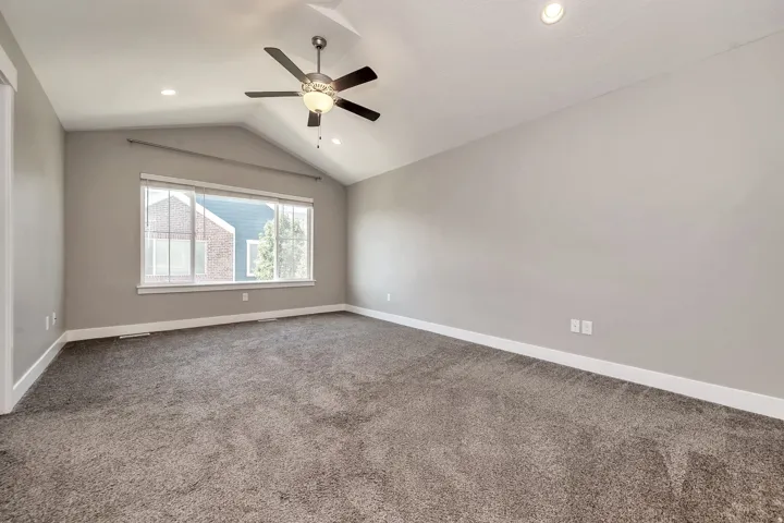 Vaulted ceiling, ceiling fan with integrated lighting, recessed lighting, large window with blinds, and neutral tone carpeting
