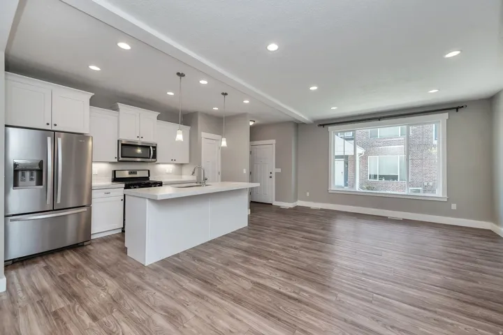 Open-concept living area featuring wood-finish flooring, recessed lighting, and a kitchen with white cabinetry
