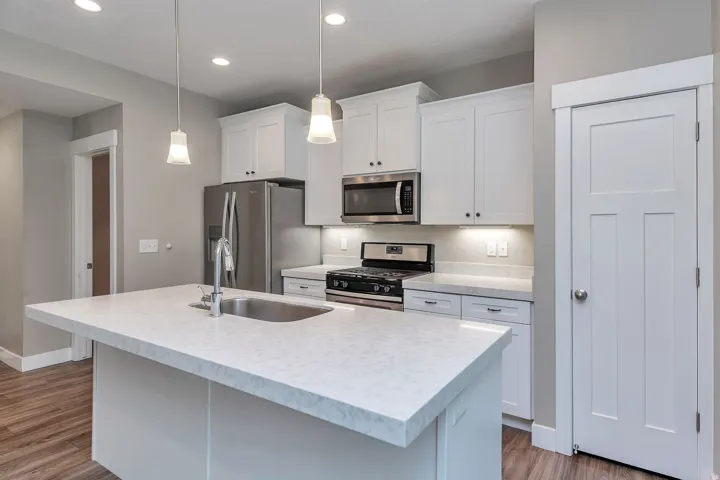 Central kitchen island with an undermount sink, white shaker cabinetry, stainless steel appliances, and pendant lighting