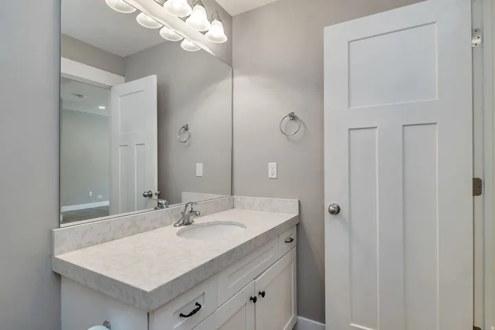 White vanity with a light-colored countertop, undermount sink, wall-mounted mirror, and overhead light fixture