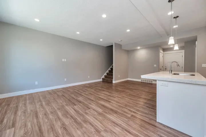 Open concept living space featuring wood-finish flooring, recessed lighting, and a kitchen island with a built-in sink