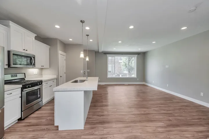 Open-concept living area with wood-finish flooring, recessed lighting, and a kitchen island with pendant lighting