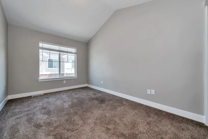 Vaulted ceiling, neutral wall tones, large window with blinds, plush carpeting, and white trim