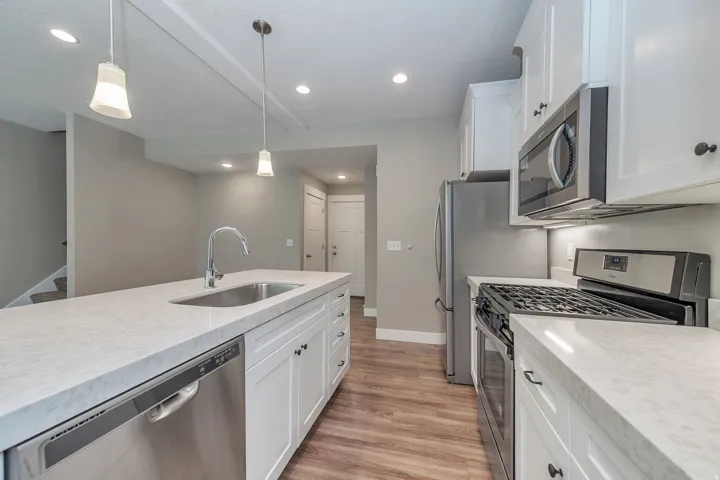 Kitchen featuring white cabinetry, light-toned countertops, stainless steel appliances, and wood-finish flooring