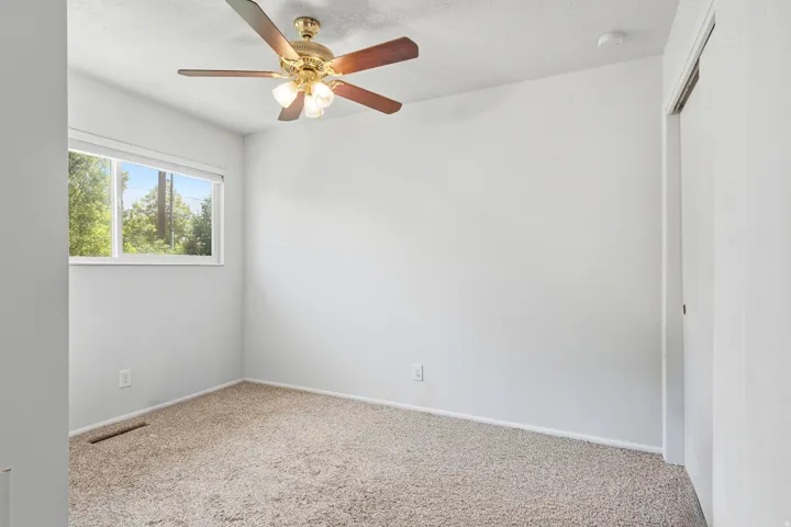 White walls, carpet flooring, window with natural light, ceiling fan with light fixture, and a white door