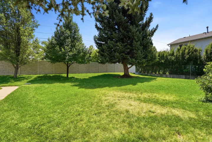 Expansive backyard with mature shade trees, lush manicured lawn, and wooden privacy fencing