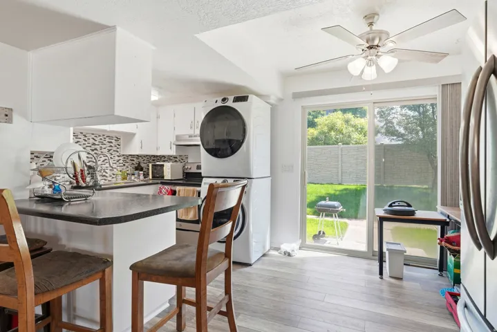 Kitchen area featuring a breakfast bar with dark countertops, white cabinetry, a tiled backsplash, and wood-finish flooring