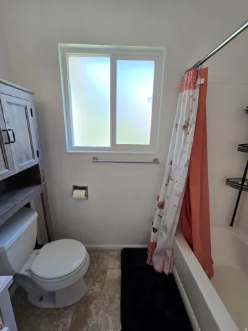 Bathroom featuring a white bathtub, toilet, and a frosted window