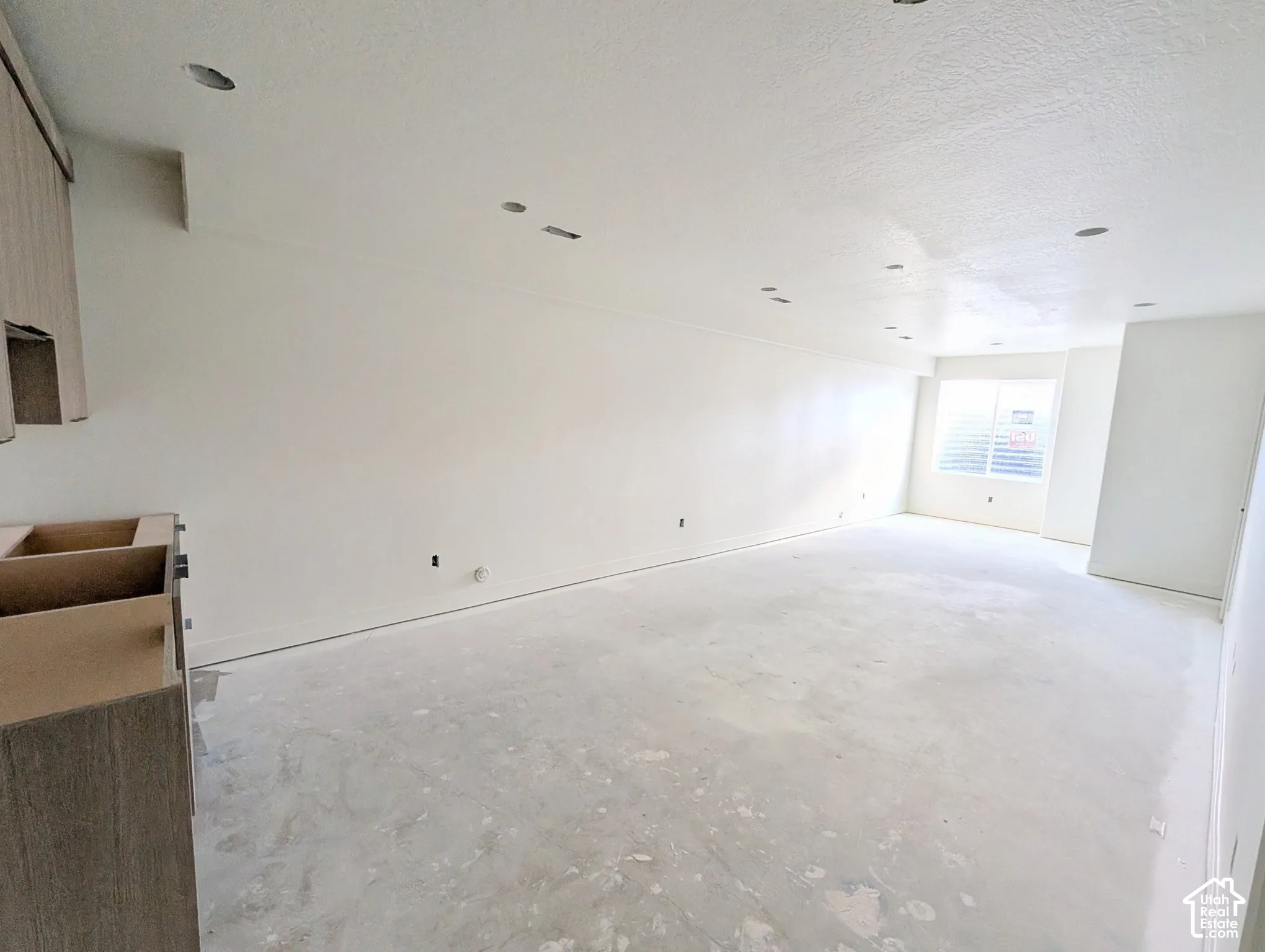 Recessed ceiling lighting, window with horizontal blinds, neutral wall finish, unfinished cabinetry, and unfinished flooring