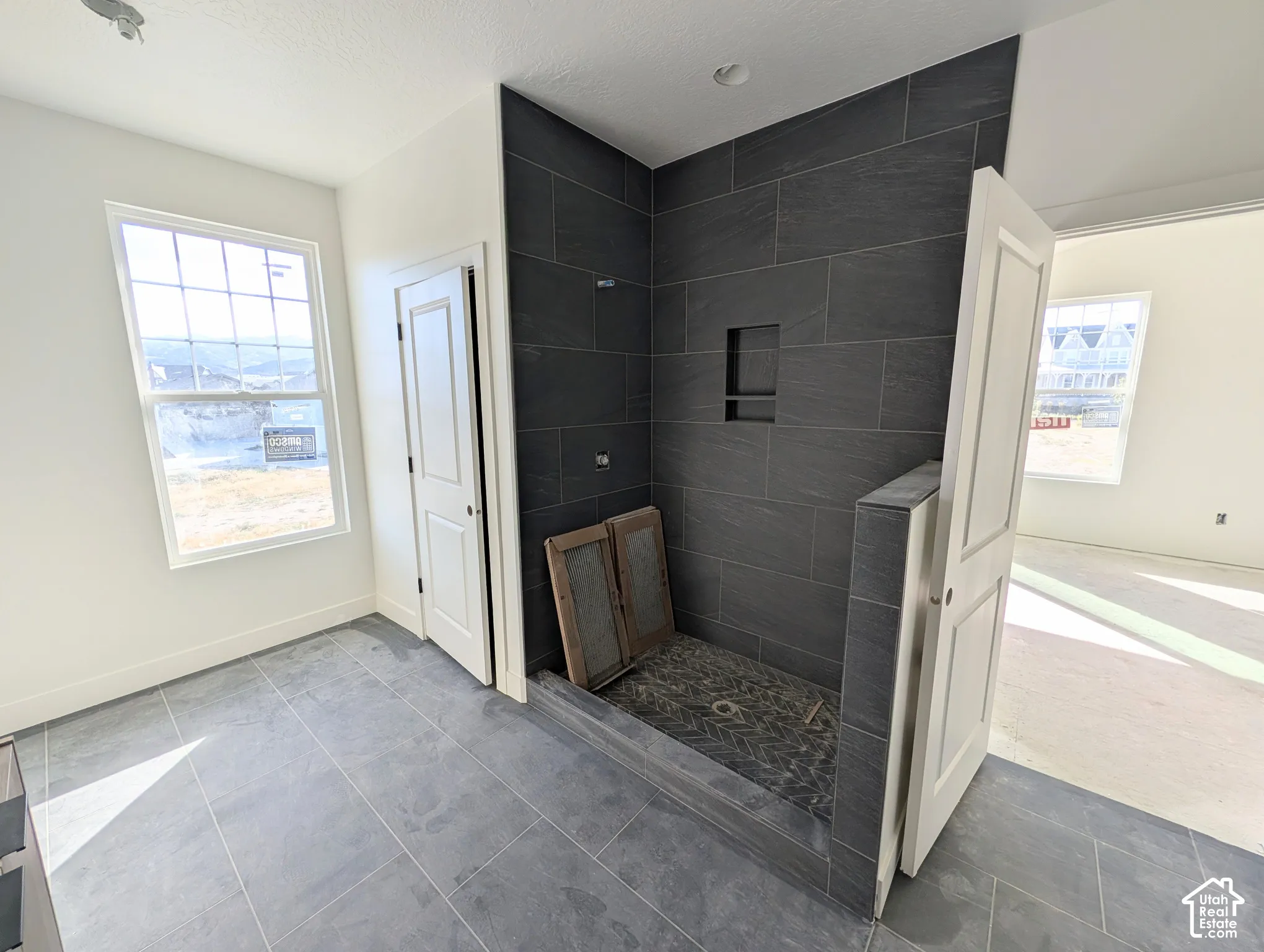 Spacious bathroom featuring large format tile flooring, a walk-in shower with dark tile surround, and a built-in shower niche