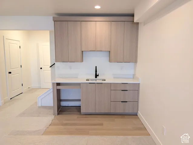 Built-in cabinetry with light wood-finish doors and drawers, white countertop, stainless steel sink, and a black gooseneck faucet