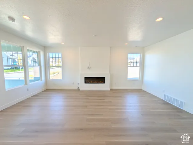 Recessed lighting, light wood-finish flooring, multiple windows, built-in electric fireplace, and white walls