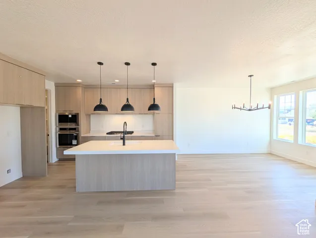 Open-concept kitchen and living area featuring light wood-finish flooring, a kitchen island with seating, pendant lighting, and an integrated oven and microwave