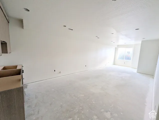 Recessed ceiling lighting, window with horizontal blinds, neutral wall finish, unfinished cabinetry, and unfinished flooring