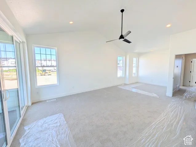Spacious primary bedroom area featuring neutral carpet flooring, abundant natural light from multiple glass doors and windows, contemporary ceiling fan with black finish, and recessed lighting throughout