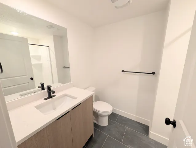 Modern bathroom featuring a wood-finish vanity with an integrated white quartz countertop and rectangular vessel sink, matte black hardware and faucet, large framed mirror with integrated lighting, and a walk-in shower with dark tile flooring and grab bar