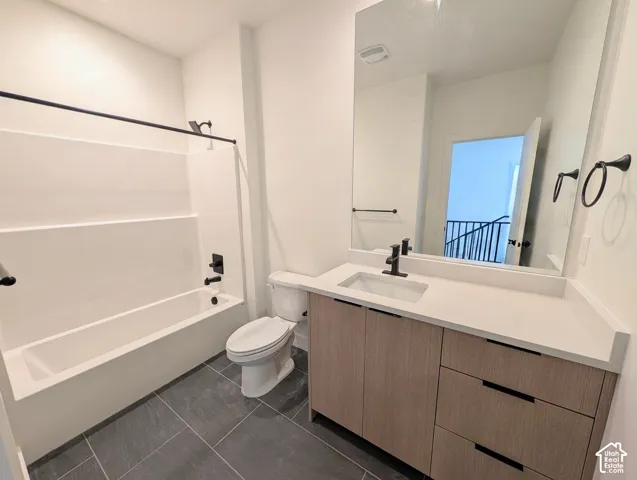 Bathroom featuring a single-basin vanity with wood-finish cabinetry, a large wall mirror, a bathtub with a shower, dark tile flooring, and matte black fixtures