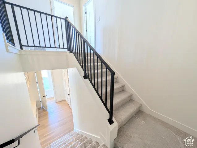 Staircase featuring carpeted treads, white risers, and black metal railings