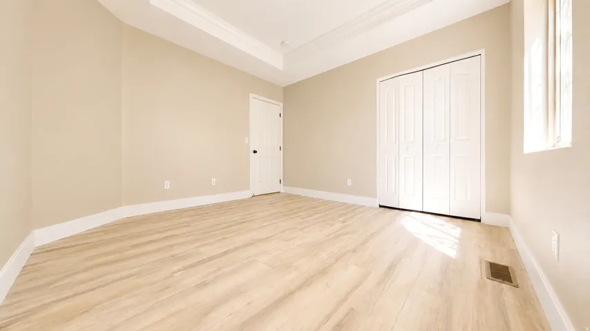 Tray ceiling with crown molding, wood-finish flooring, white bi-fold closet doors, and recessed lighting