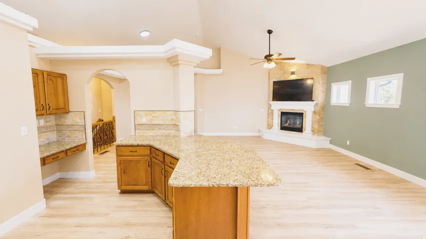 Open-concept living space with wood-finish flooring, a stone-faced fireplace with hearth, and an expansive kitchen island with a stone-finish countertop