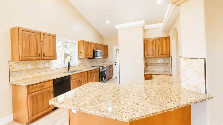 Kitchen featuring wood-finish cabinetry, granite countertops, tile backsplash, stainless steel appliances, and a vaulted ceiling