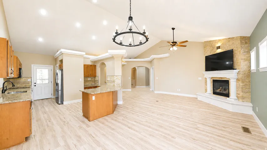 Vaulted ceilings with recessed lighting, wood-finish flooring, stone-clad fireplace, kitchen island with stone countertop, and wood cabinetry