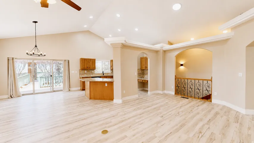 Vaulted ceiling with recessed lighting and a chandelier, wood-finish flooring, sliding glass doors to outdoor deck, integrated kitchen island, and an arched entry with decorative railing