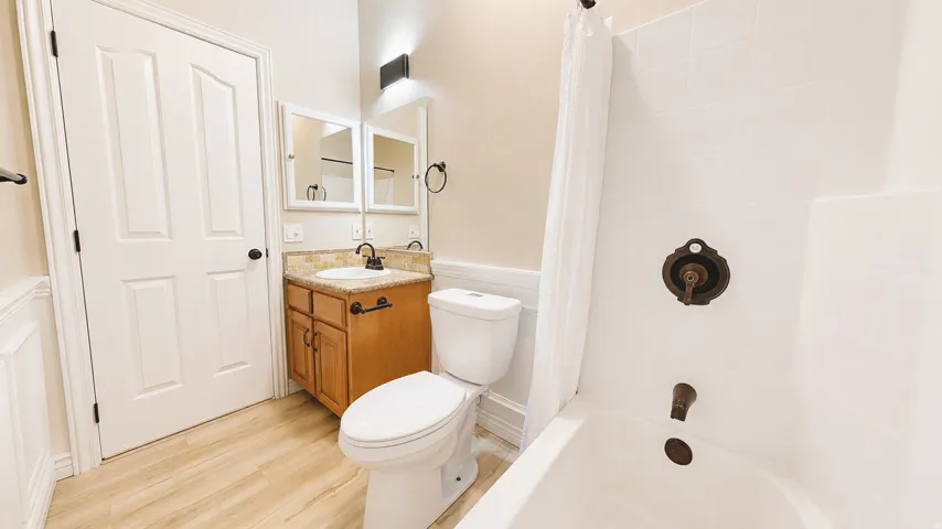 Wood-finish flooring, wood vanity with a stone countertop, white paneled door, and a white tiled shower/tub combination