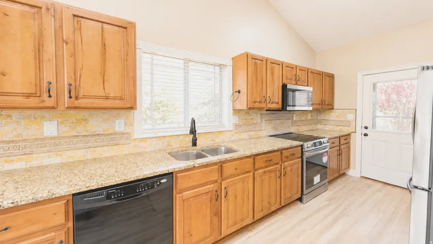 Vaulted ceiling, wood-finish cabinetry, stone countertops, double basin sink, and stainless steel appliances