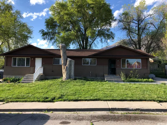 Duplex property featuring a brown exterior, dual front entrances with steps, and a grassy front yard